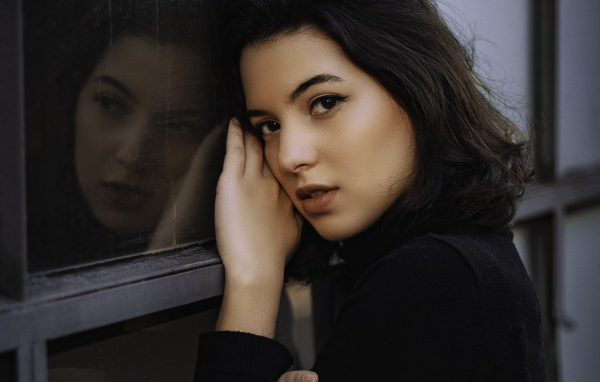 Красивая кареглазая девушка стоит у окна