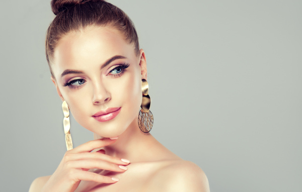 Красивая девушка шатенка с золотыми серьгами в ушах на сером фоне