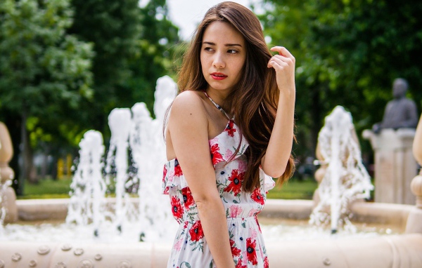 Красивая шатенка в цветастом платье у фонтана летом