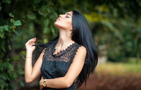 Красивая брюнетка в черном платье с закрытыми глазами в парке