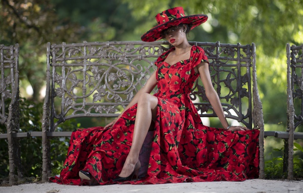 Красивая темнокожая девушка в красном платье сидит на лавке