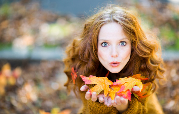 Красивая девушка сдувает листья с ладоней