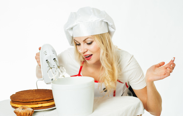 Красивая девушка повар взбивает крем для торта миксером