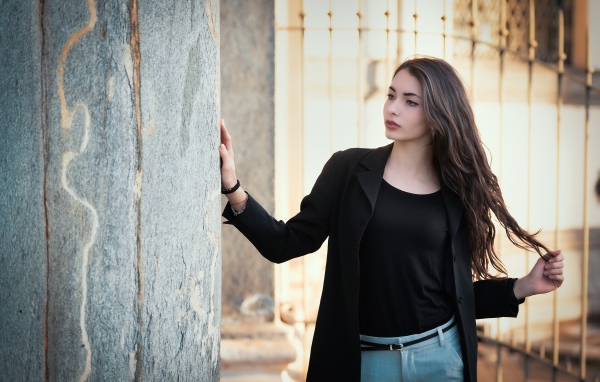 Красивая девушка в черном пиджаке стоит у стены
