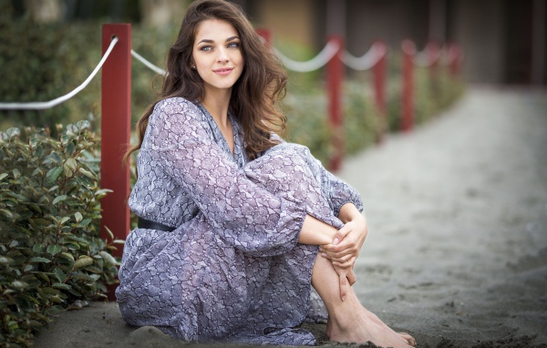 Красивая девушка в платье сидит на песке