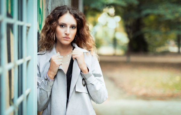 Красивая девушка в сером плаще у стены