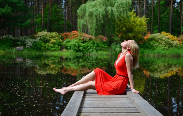 Красивая девушка сидит в красном платье на мосту