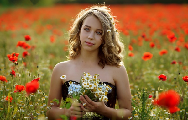 Красивая девушка с букетом ромашек на поле с маками