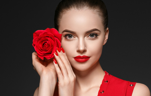 Красивая девушка с красной розой у лица на сером фоне