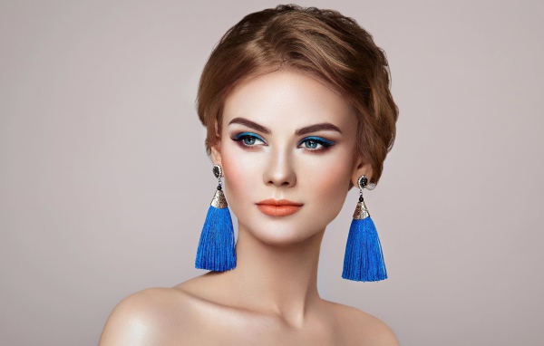 Красивая девушка с синими сережками на сером фоне