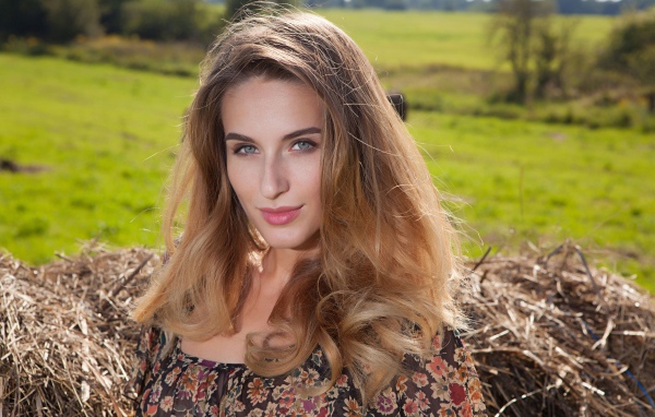 Красивая девушка с серыми глазами стоит у сена