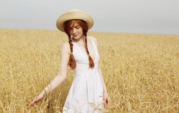 Красивая рыжеволосая девушка гуляет по полю с пшеницей