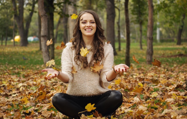 Красивая улыбающаяся девушка сидит на земле с желтыми листьями