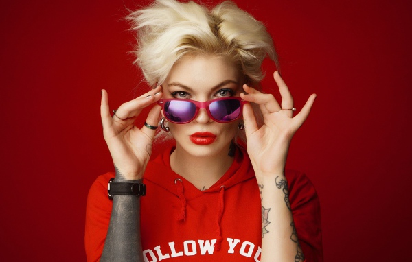 Яркая блондинка с татуировками на руках на красном фоне