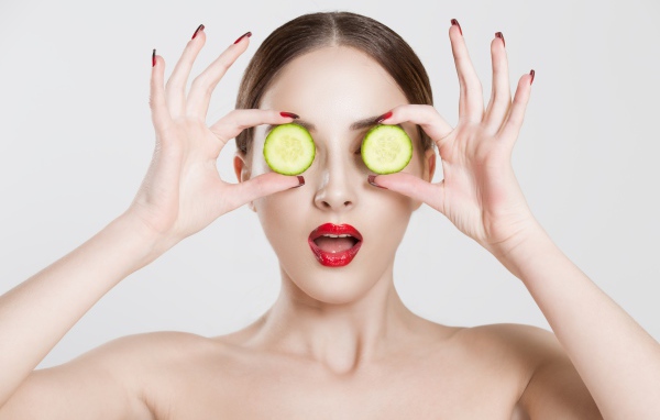 Яркая девушка с огурцами у глаз на сером фоне
