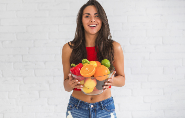 Брюнетка с миской фруктов на фоне стены