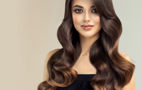 Милая кареглазая девушка с красивыми длинными волосами на сером фоне