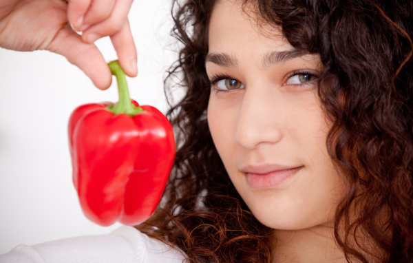 Лицо девушки с красным сладким перцем в руке крупным планом