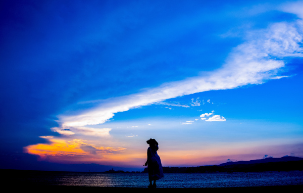 Девушка в шляпе смотрит на закат на берегу моря