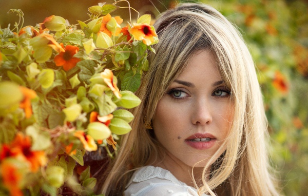 Зеленоглазая блондинка у забора с цветами 