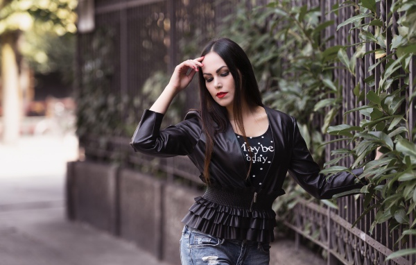 Длинноволосая брюнетка в черной куртке у забора