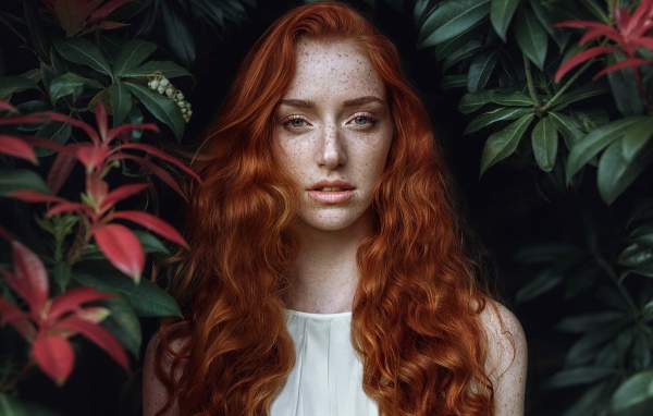 Рыжеволосая девушка с веснушками на лице на фоне кустов 