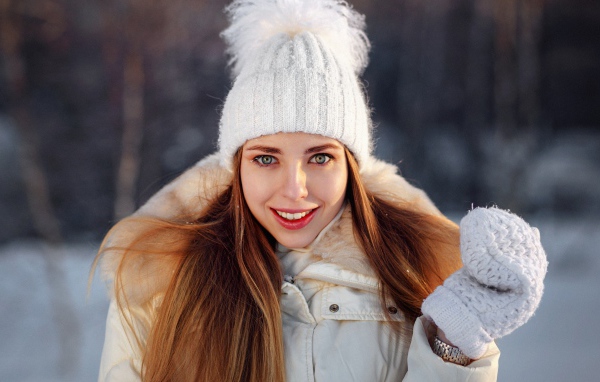 Улыбающаяся девушка в теплой шапке и варежках зимой