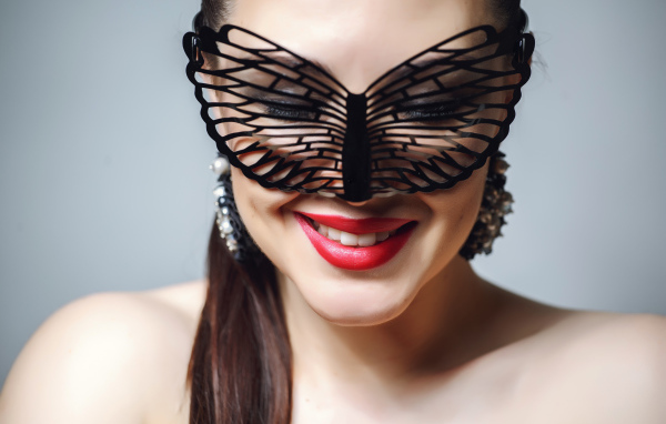 Улыбающаяся девушка в черной маске на сером фоне