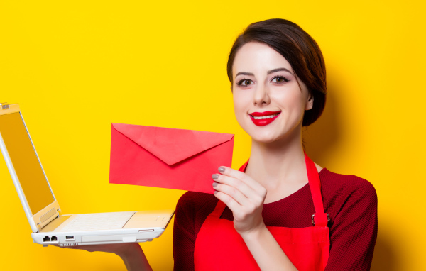 Улыбающаяся девушка с ноутбуком и конвертом в руках на желтом фоне