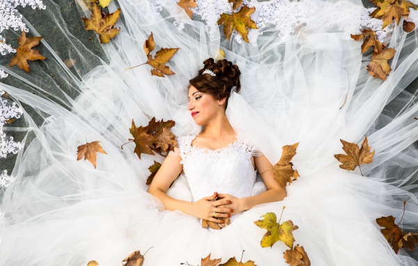 Девушка невеста в белом платье лежит с желтыми листьями