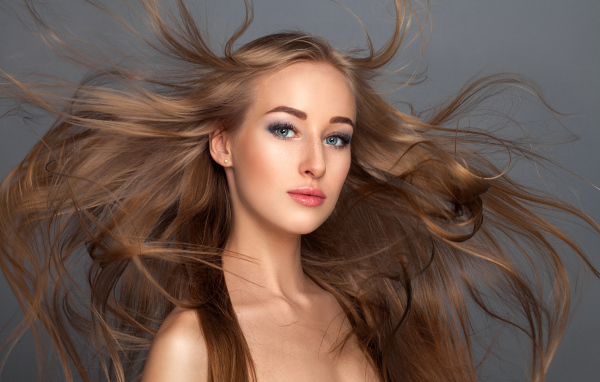 Ветер развивает волосы красивой девушке на сером фоне