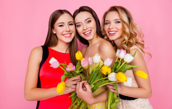 Три красивые девушки с букетами тюльпанов на розовом фоне