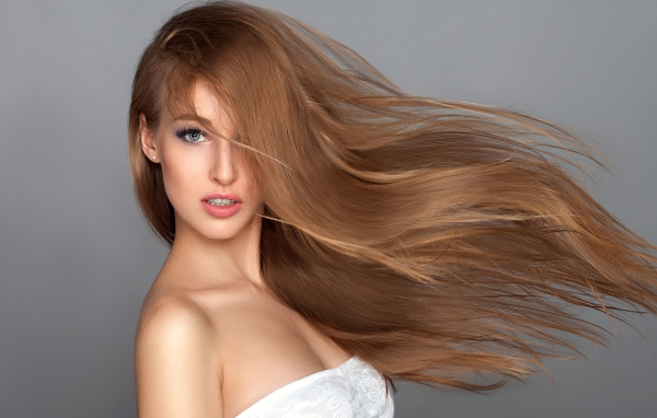 Ветер развивает волосы красивой девушки на сером фоне