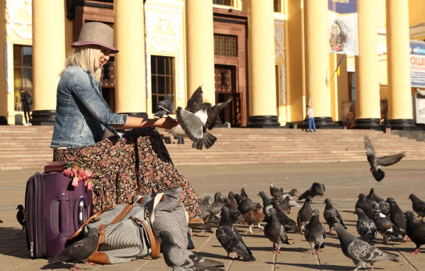 Молодая девушка кормит голубей на вокзале