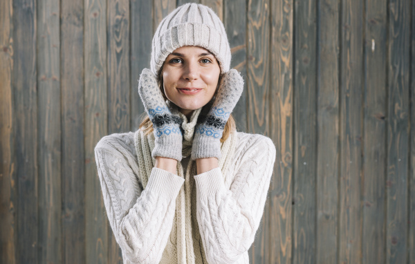 Молодая девушка на шапке, варежках  и теплой шапке на фоне забора