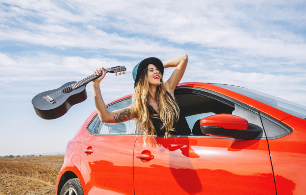 Молодая девушка с гитарой в красной машине летом