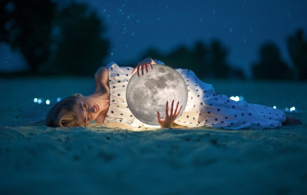 Молодая девушка с луной в руках лежит на песке