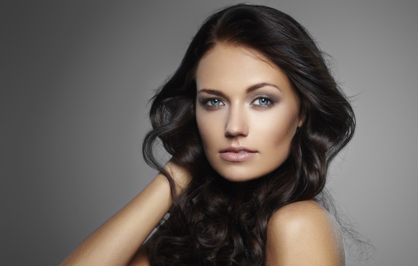 Молодая настоящая голубоглазая длинноволосая брюнетка на сером фоне