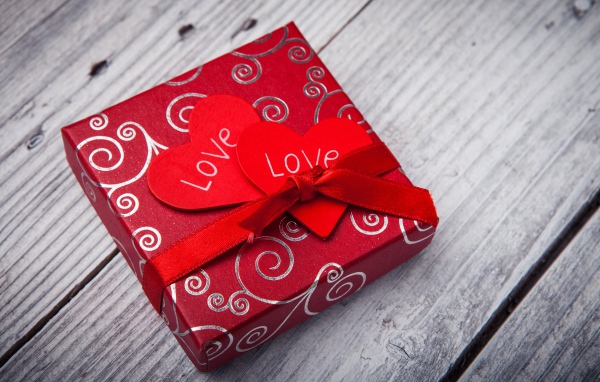 Подарок с красными сердечками на деревянном столе 