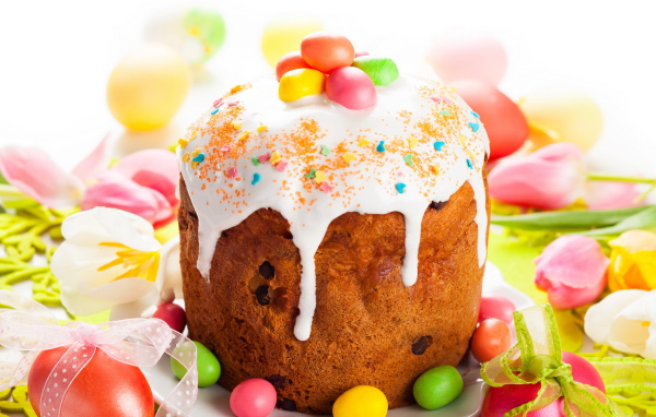 Красивый пасхальный кулич с белой глазурью и конфетами на столе с яйцами