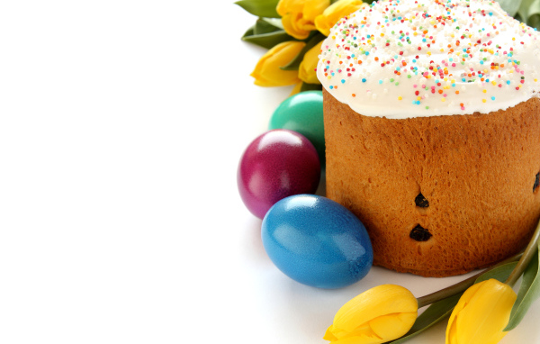 Красивый праздничный кулич с желтыми тюльпанами и крашеными яйцами на белом фоне к Пасхе