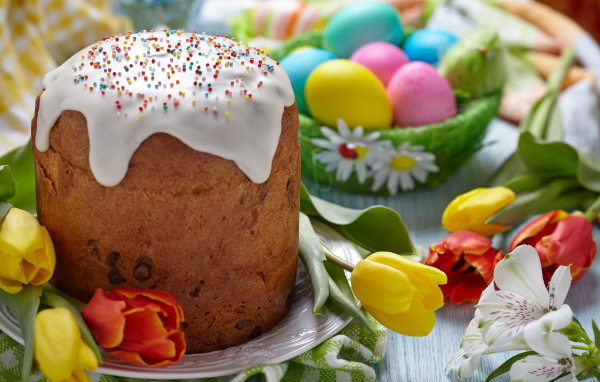 Пасхальный кулич на столе с тюльпанами и крашеными яйцами