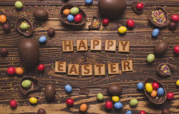 Надпись на английском Счастливой Пасхи на столе с шоколадными яйцами и конфетами