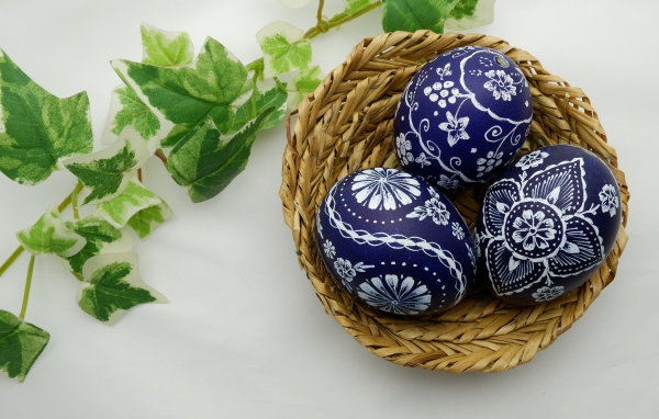 Три раскрашенных яйца в корзинке на столе с веткой 