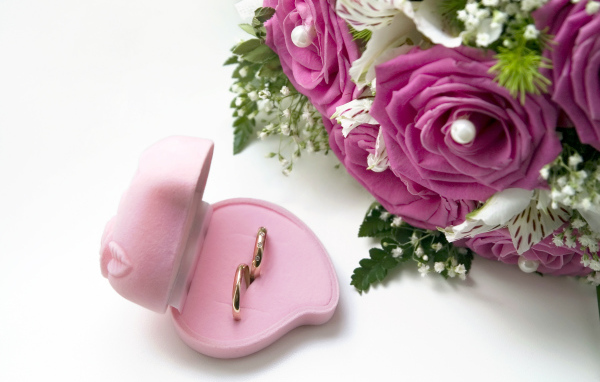 Два обручальных кольца в коробочке на белом фоне с букетом роз