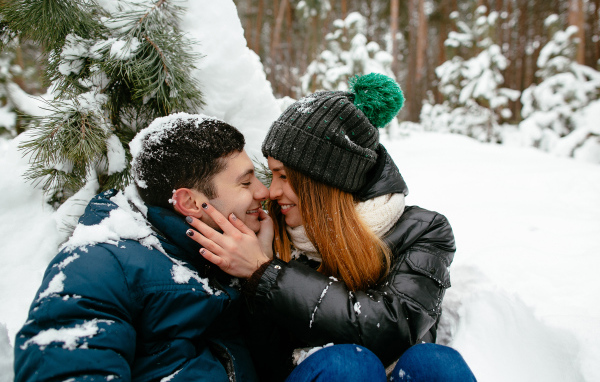 Влюбленная пара сидит под заснеженной еловой веткой зимой
