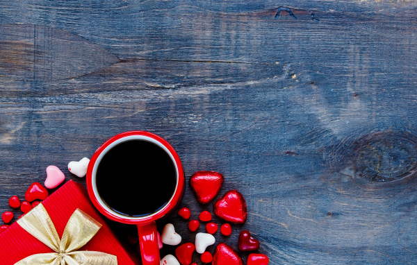 Красная чашка кофе, сердечки и подарок на деревянном фоне