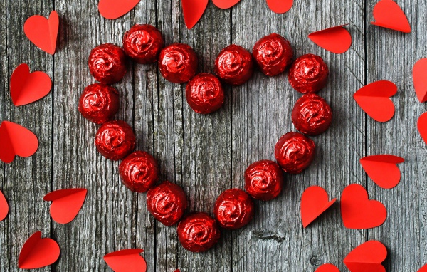 Красное сердце из конфет на деревянном фоне с бумажными сердечками