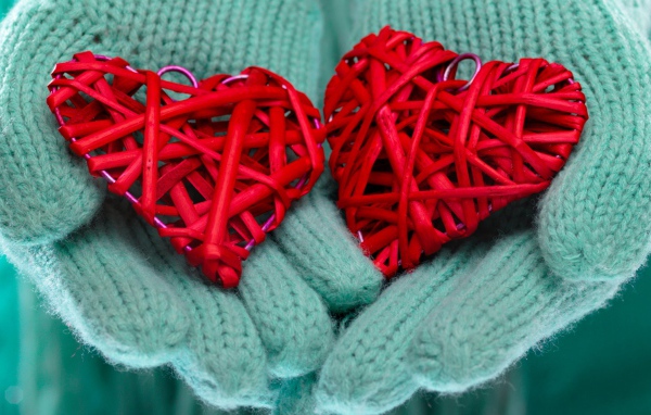 Два плетеных красных сердца лежать на руках в варежках