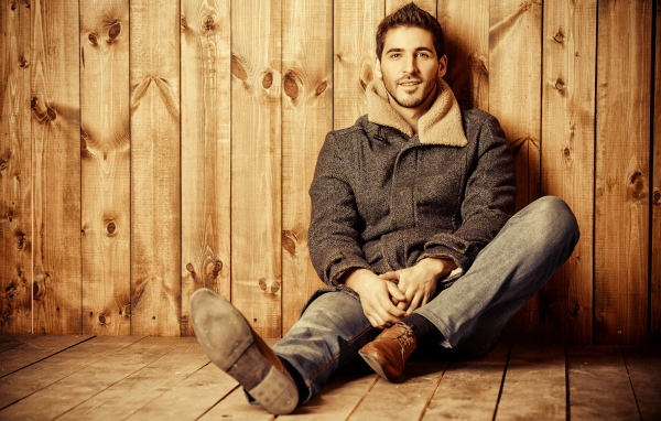 Молодой мужчина в пальто сидит у стены